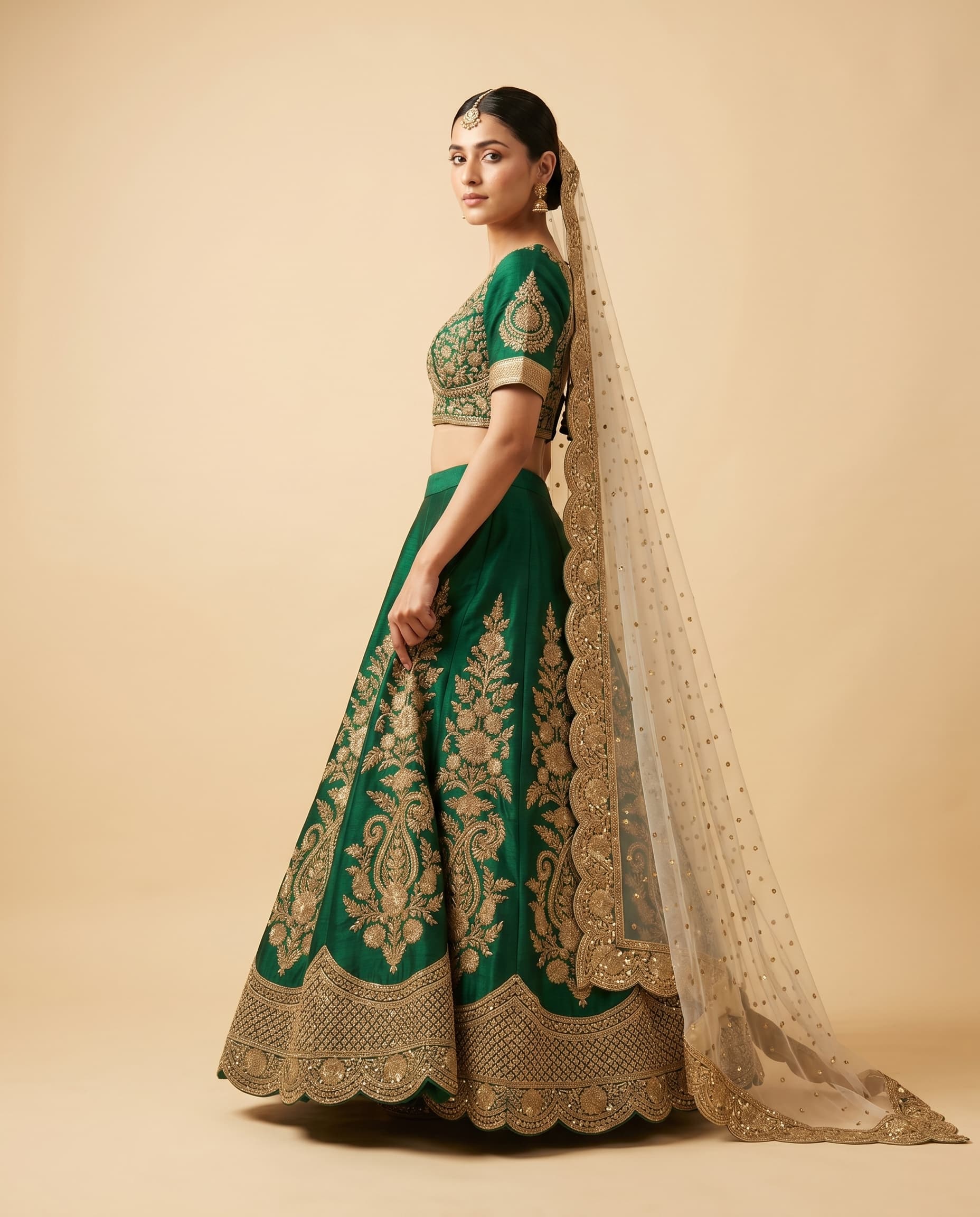 Editorial bridal portrait — a model wearing an emerald silk lehenga with gold zari embroidery and an ivory net dupatta on a seamless cream studio backdrop, rendered by Kraftr.